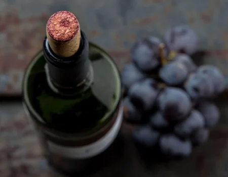 artica+i. Imagen para la galería interior del caso de éxito (nuestros proyectos) "POLYRESWINE. Proyecto de I+D orientado a aplicar nuevas técnicas basadas en resinas de intercambio iónico/absorbentes para eliminar compuestos indeseables en el vino", mostrando el detalle de una botella de vino con un racimo de uva